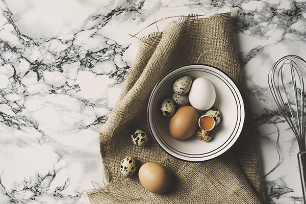 Fresh organic eggs and quail eggs in ceramic bowl on marble countertop. Top view shot.
