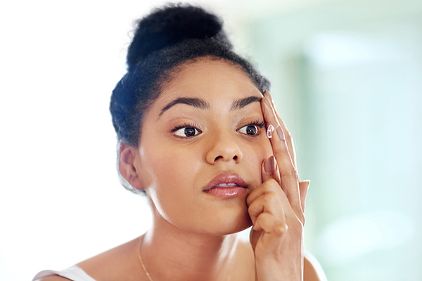 Shot of a young woman putting in contact lenses at home