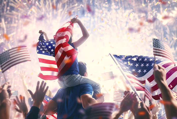 Patriotic holiday. Child sitting on shoulders of her father and holding the Flag of the USA. America celebrate 4th of July.
